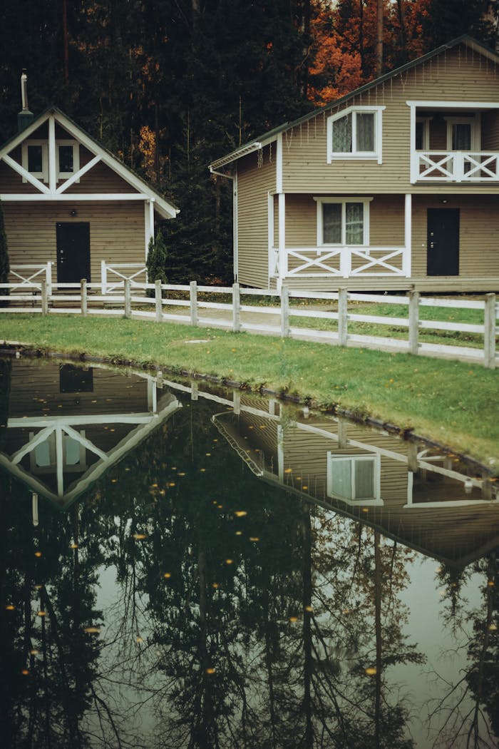 Charming rustic cabins reflected in a serene pond during fall, surrounded by forest.